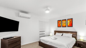A modern bedroom with a large bed, a flat-screen TV, a wooden dresser, and three wall-mounted paintings.