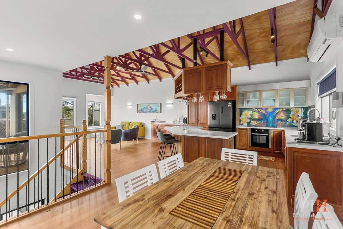 A modern kitchen with wooden cabinets, a central island, and a dining area with a wooden table and chairs.