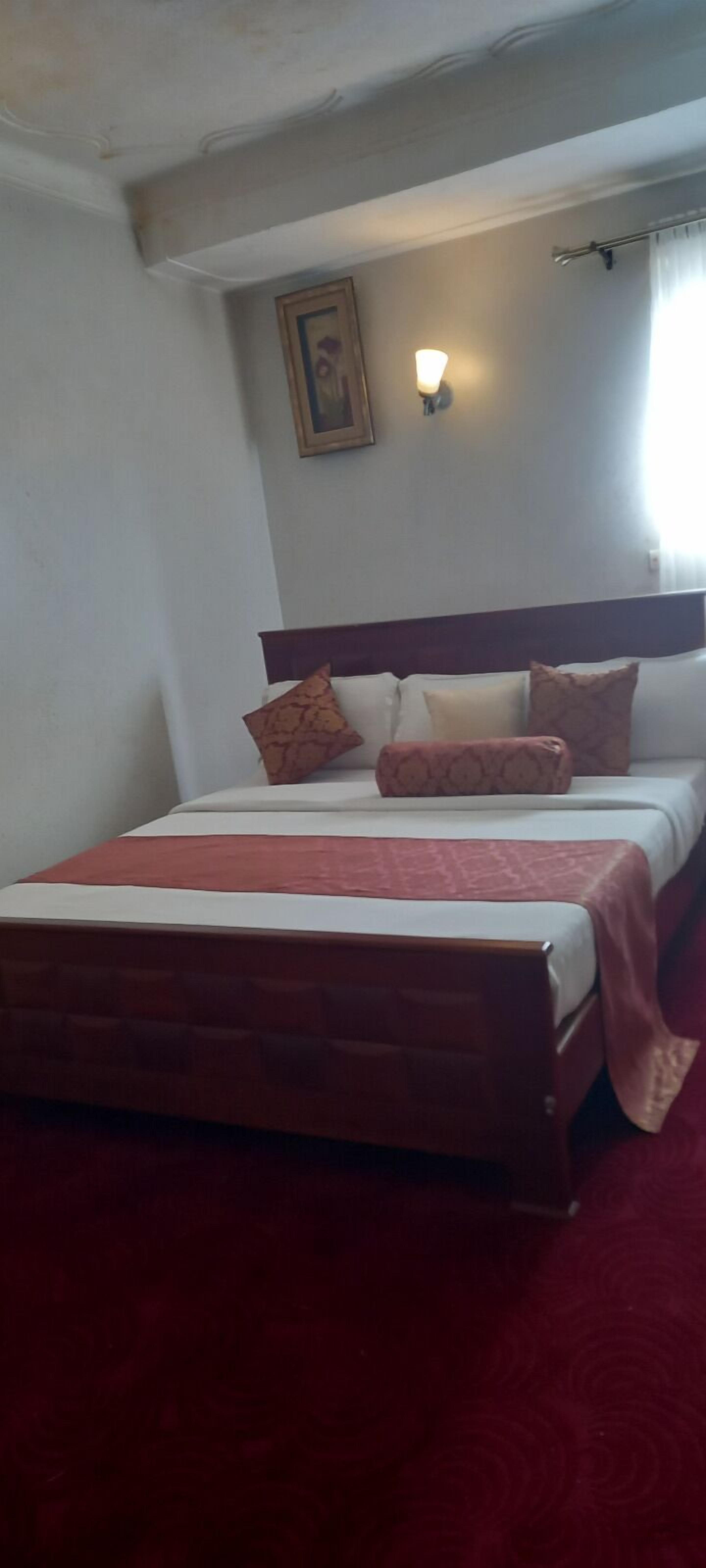 Habitación de hotel estándar con una cama individual, cabecera, luz de pared y ventana con cortinas.