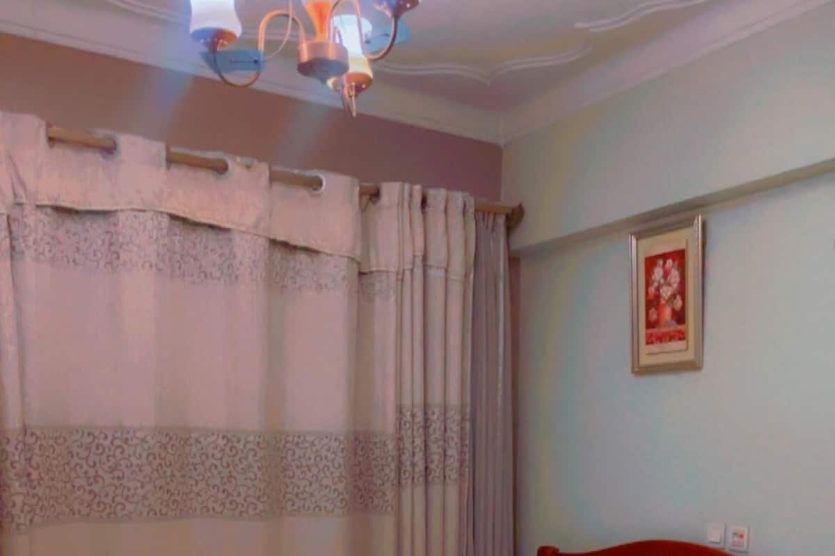 Una cama bien tendida con cabecera de madera, una mesita de noche y una lámpara fijada a la pared.