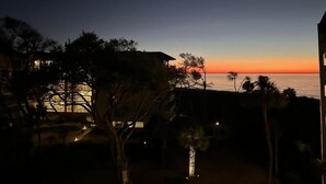 Une vue sur la côte au crépuscule, avec un bâtiment et des arbres au premier plan.