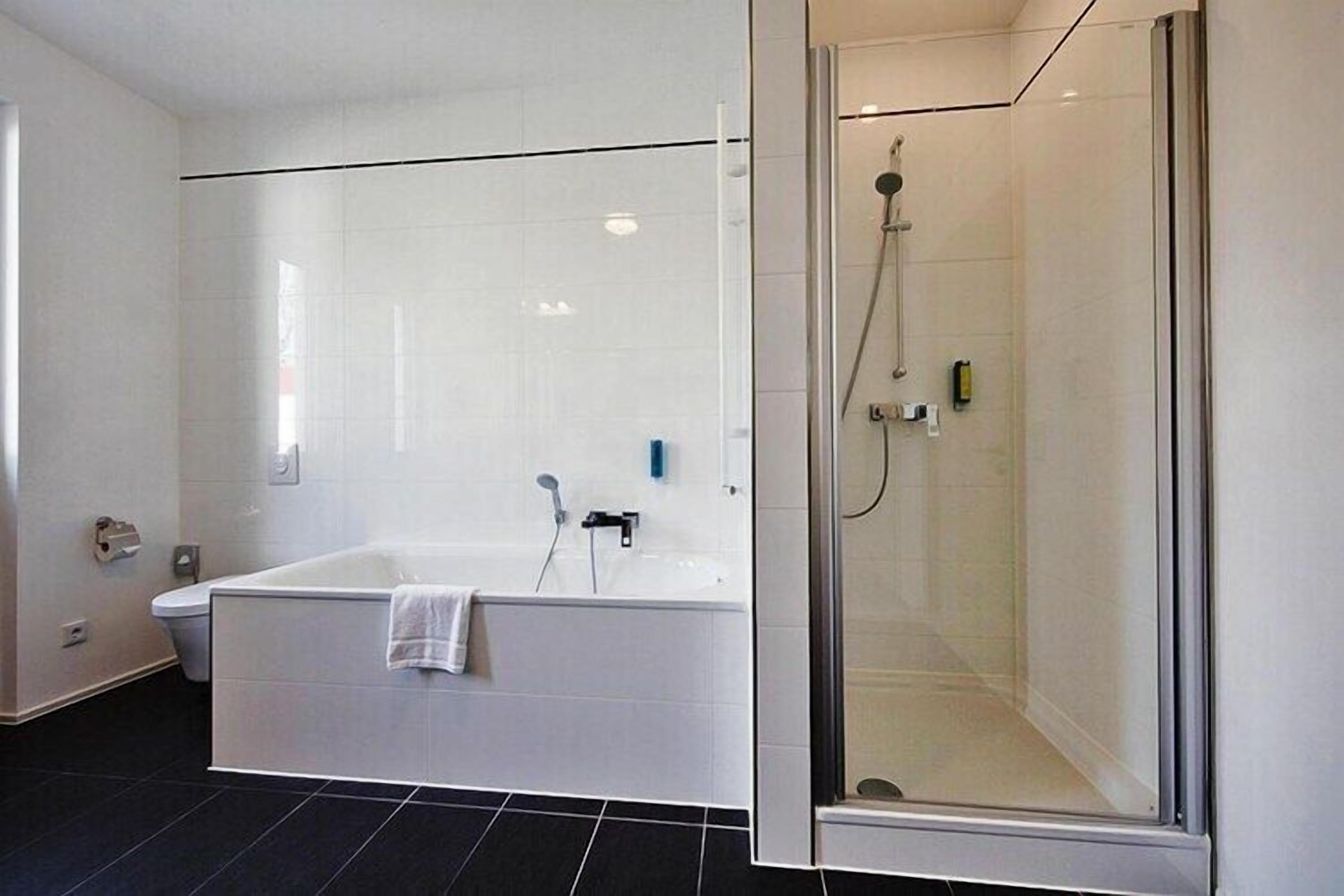 Un baño moderno con una bañera blanca, cabina de ducha con paredes de vidrio y suelo de baldosas negras.