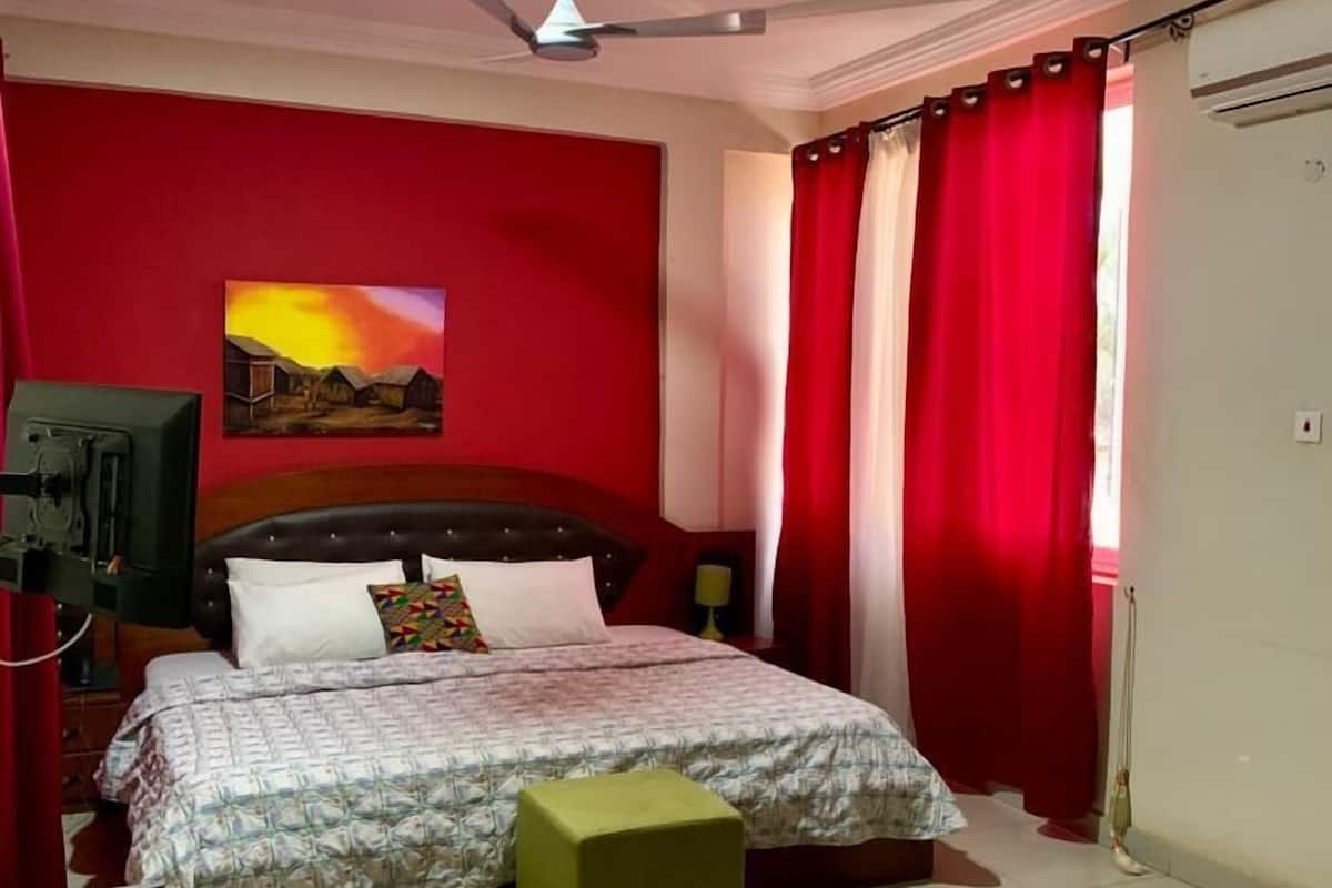 Quarto com cama, ventilador de teto, pintura, cortina vermelha e piso de azulejos.