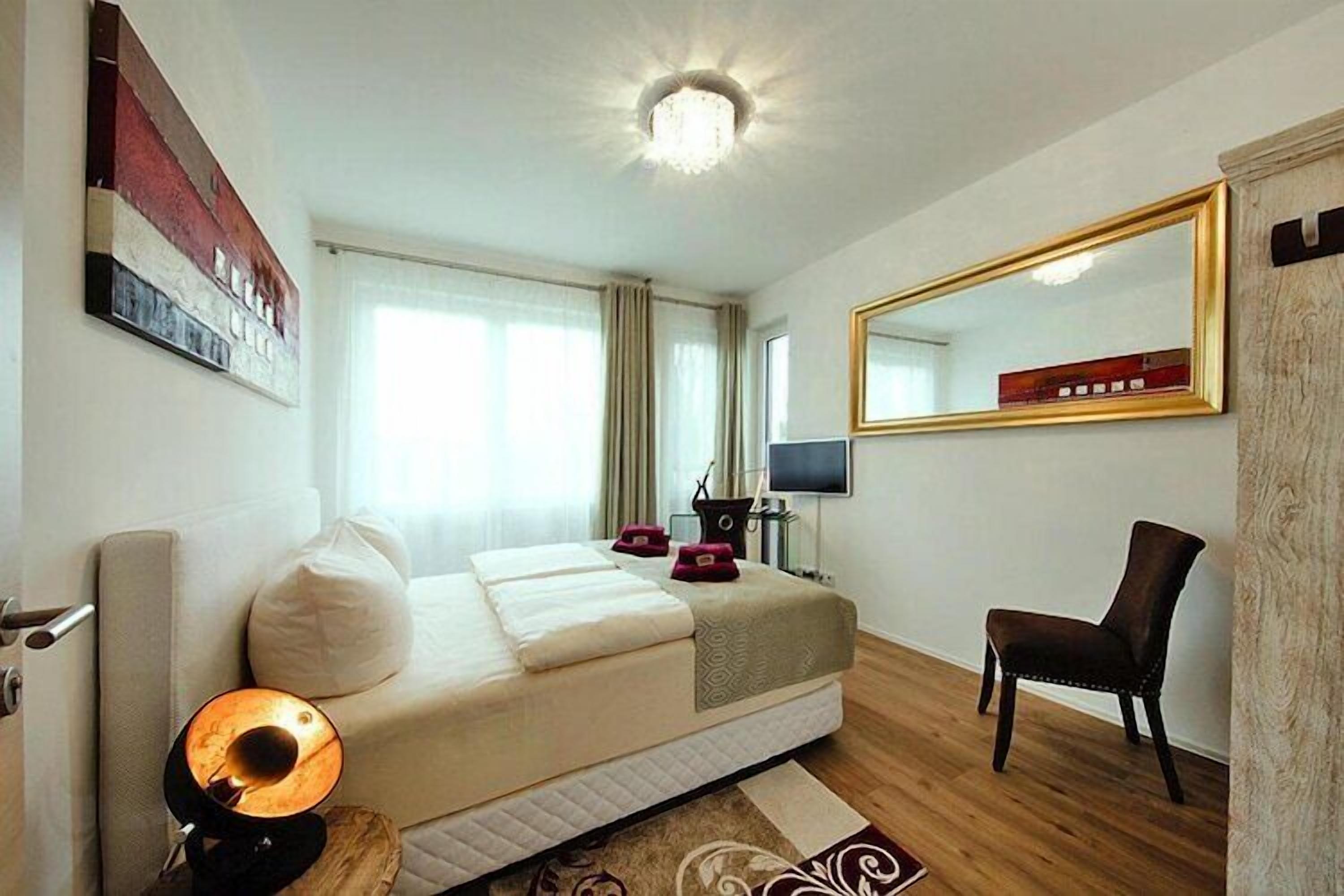 Una camera d'hotel con un letto, una scrivania, una sedia, un televisore e un grande specchio.