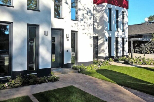 Un bâtiment moderne à la façade blanche, doté de portes numérotées et d’une pelouse bien entretenue.