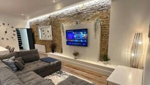 Een moderne woonkamer met een modulaire bank, een flatscreen-televisie bevestigd aan een gestructureerde muur en een kleine tafel met een lamp.