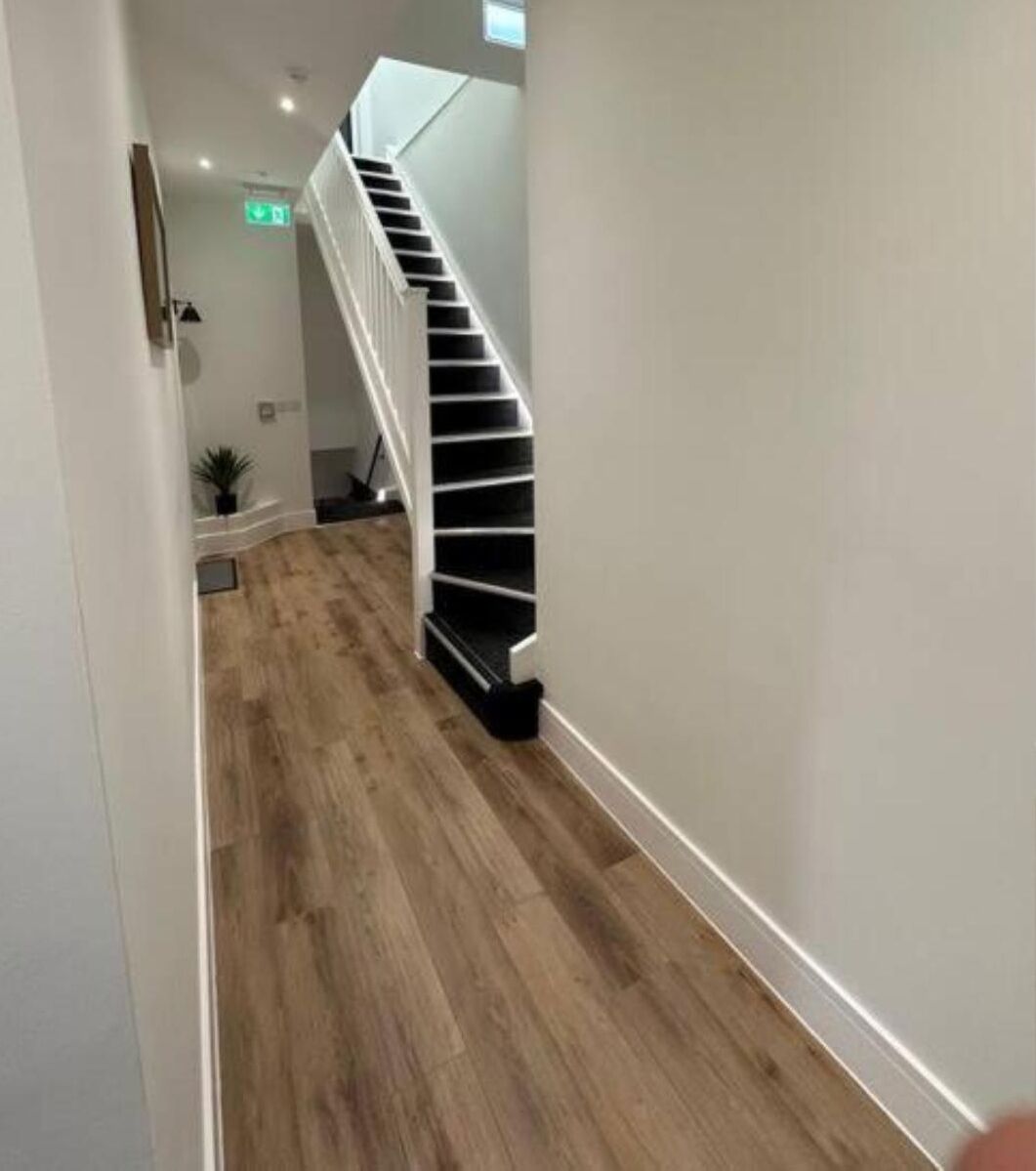 Un couloir au plancher de bois menant à un escalier blanc doté d’une main courante.