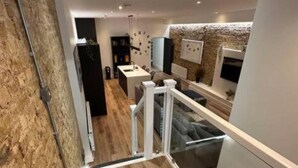 Een moderne keuken met een houten vloer, een eethoek met tafel en stoelen, en een trap met glazen leuning.