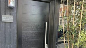 Een donkerhouten deur met een verticale handgreep en een klein bord erboven.