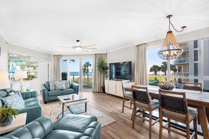A spacious living room with a ceiling fan, a dining area with wooden chairs, a TV, and a view of the ocean.