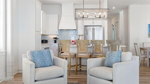 Una cocina moderna con armarios blancos, un refrigerador de acero inoxidable y un comedor con sillas de colores claros y una mesa.