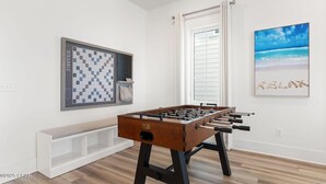 Una habitación con una mesa de fútbol de mesa, un tablero de ajedrez y un cuadro con motivos playeros.