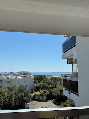 A view from a balcony overlooking a coastal area with buildings, a parking lot, and a clear sky.
