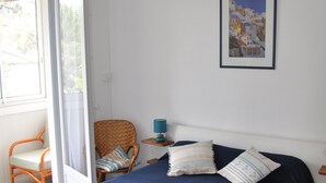 Un dormitorio con una cama, dos sillas, una mesita de noche con una lámpara y un cuadro en la pared.