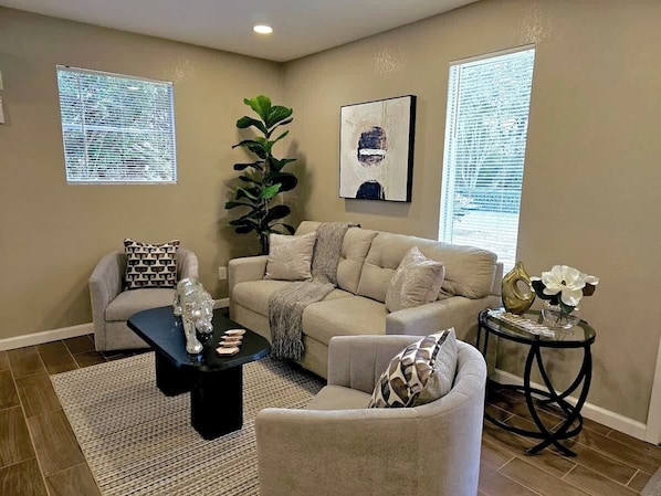 A living room with a beige sofa, a black coffee table, a side table, and a potted plant.