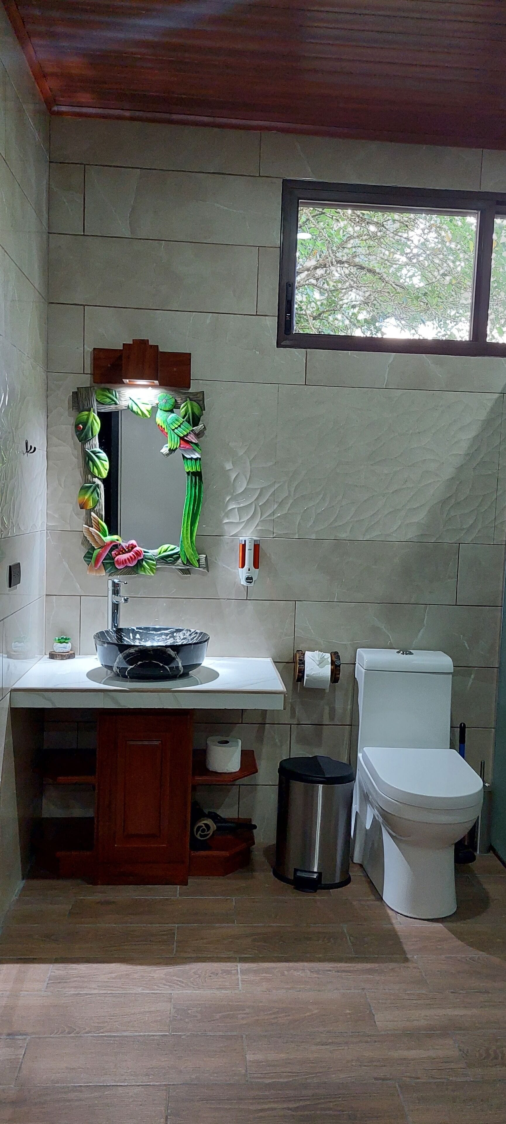 A bathroom with a white toilet, a sink with a decorative mirror, and a window above the toilet.