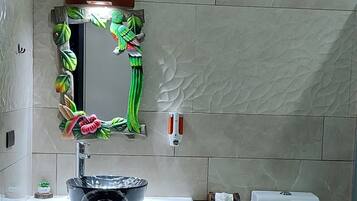 A bathroom with a white toilet, a sink with a decorative mirror, and a window above the toilet.