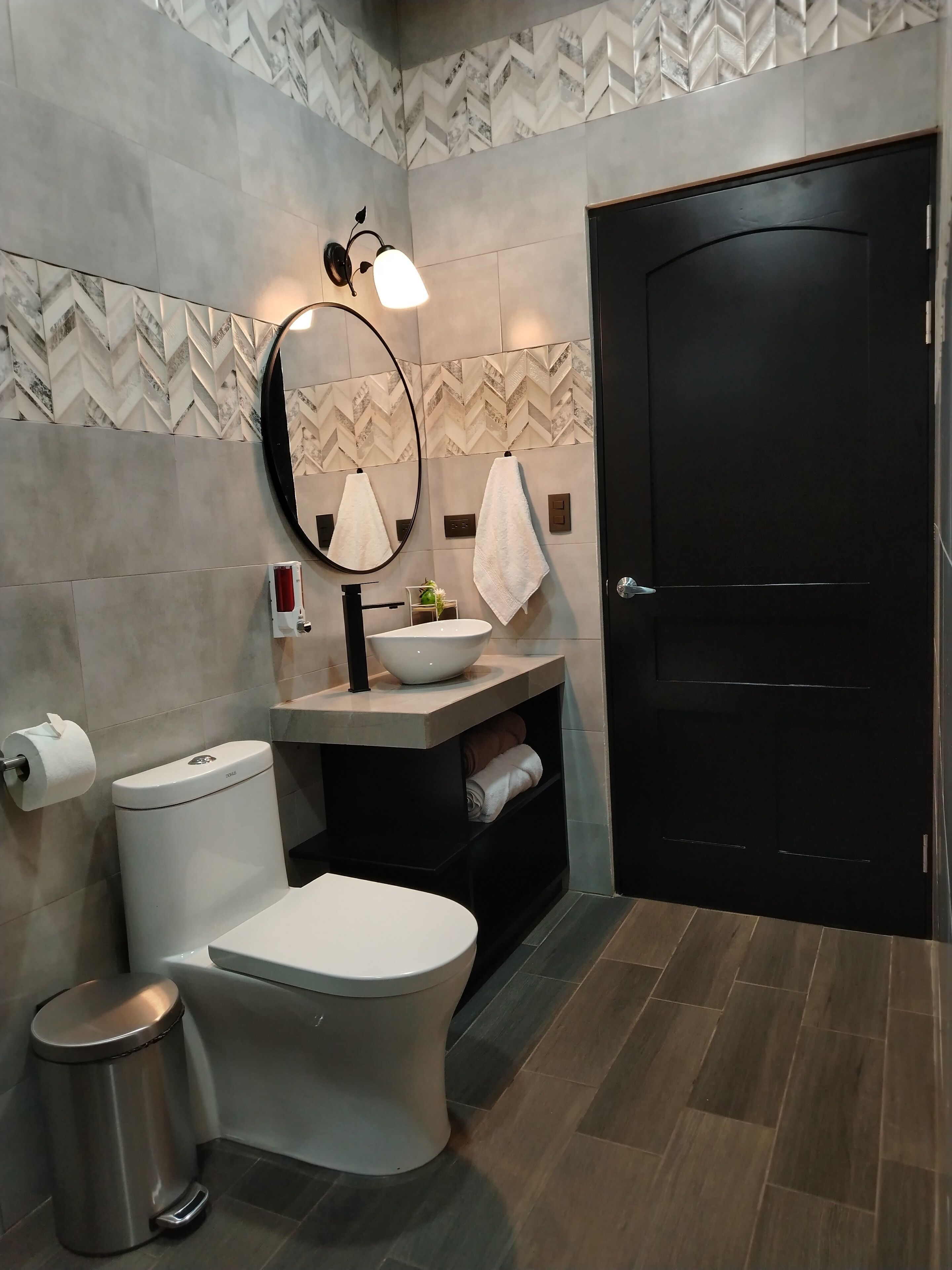 A modern bathroom with a toilet, bidet, sink, mirror, towel rack, and a trash bin.