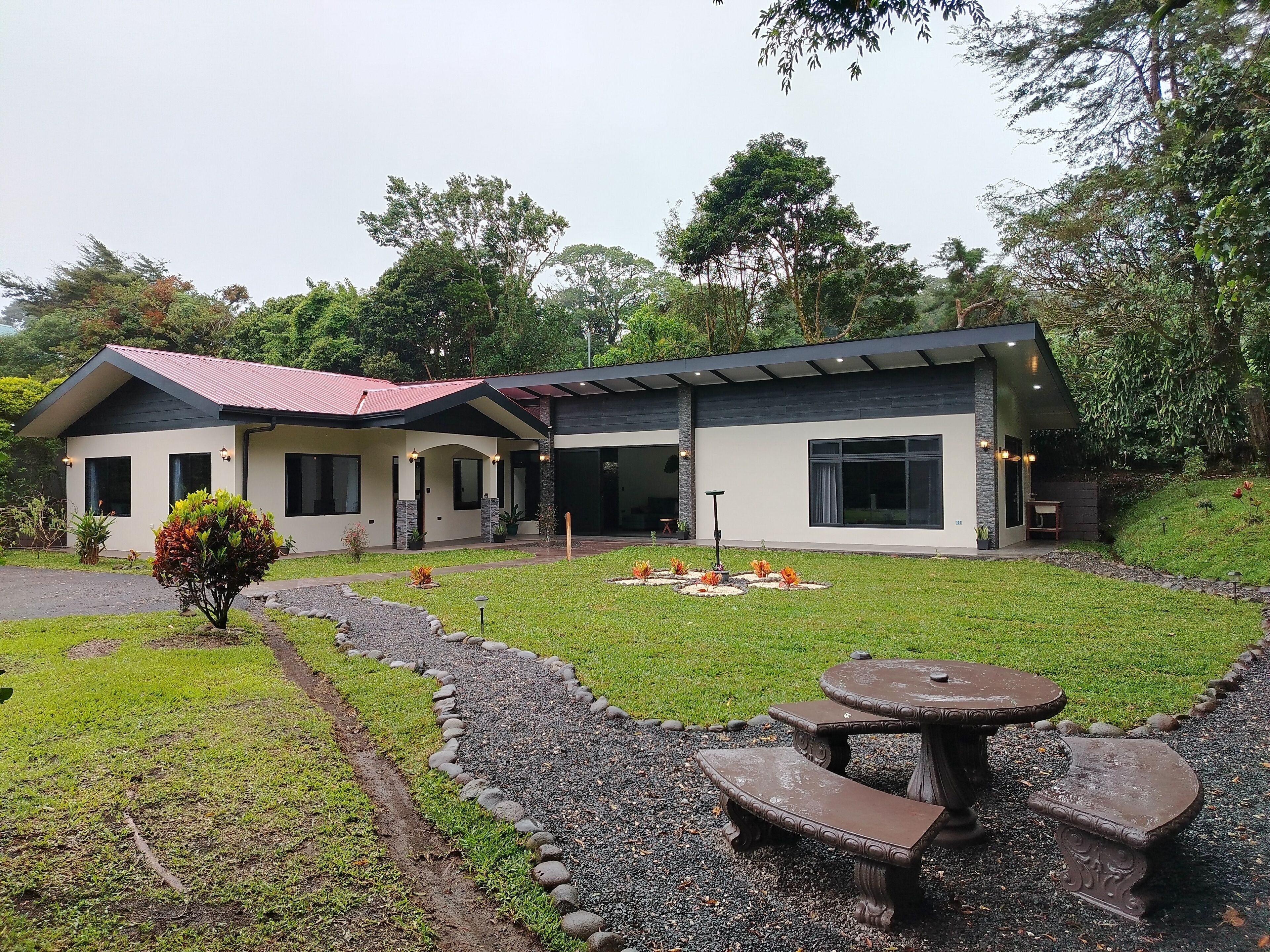 Een modern huis met twee verdiepingen, met een overdekte patio, omringd door een verzorgd gazon en een tuin.