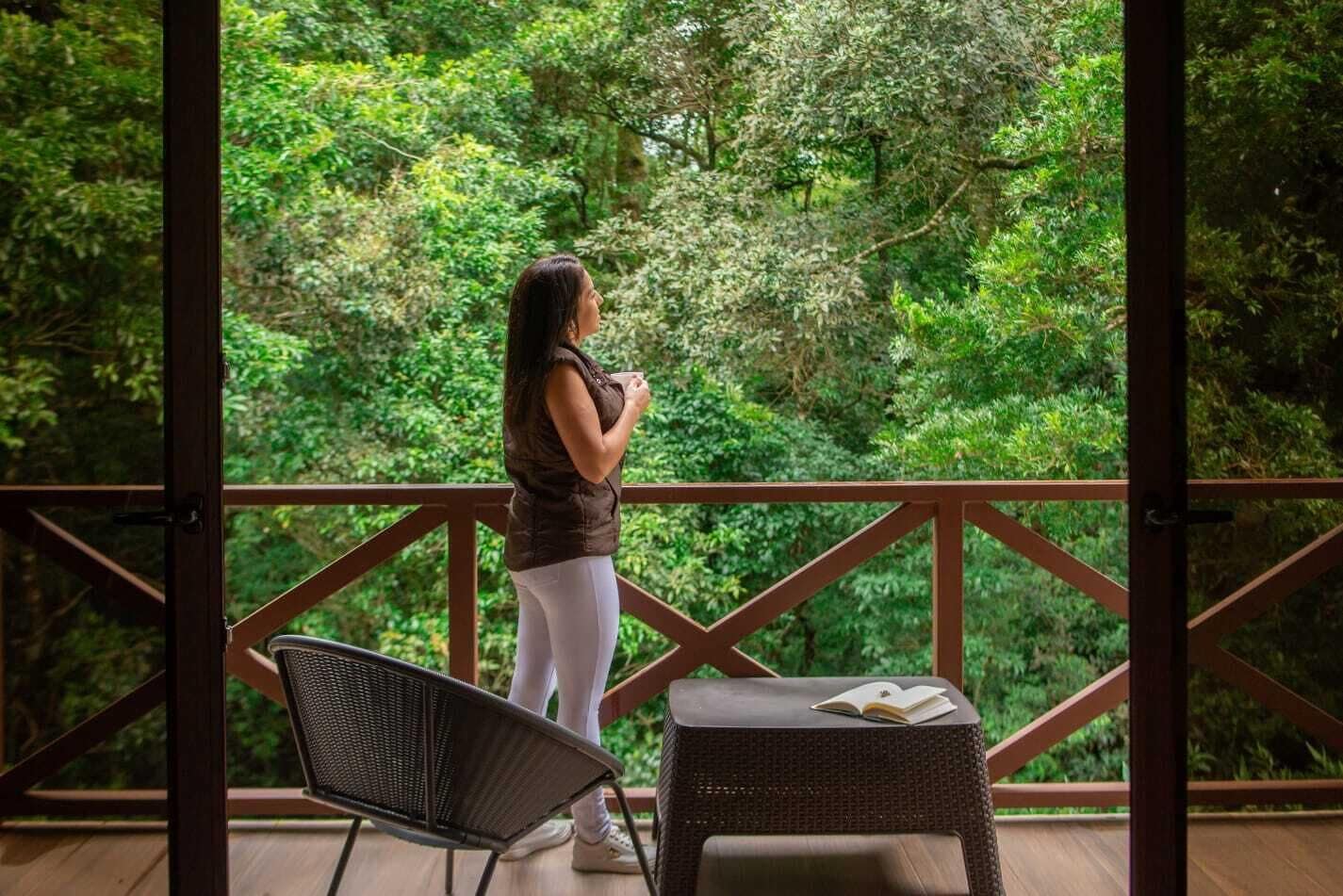 A person standing on a balcony with a view of dense greenery.