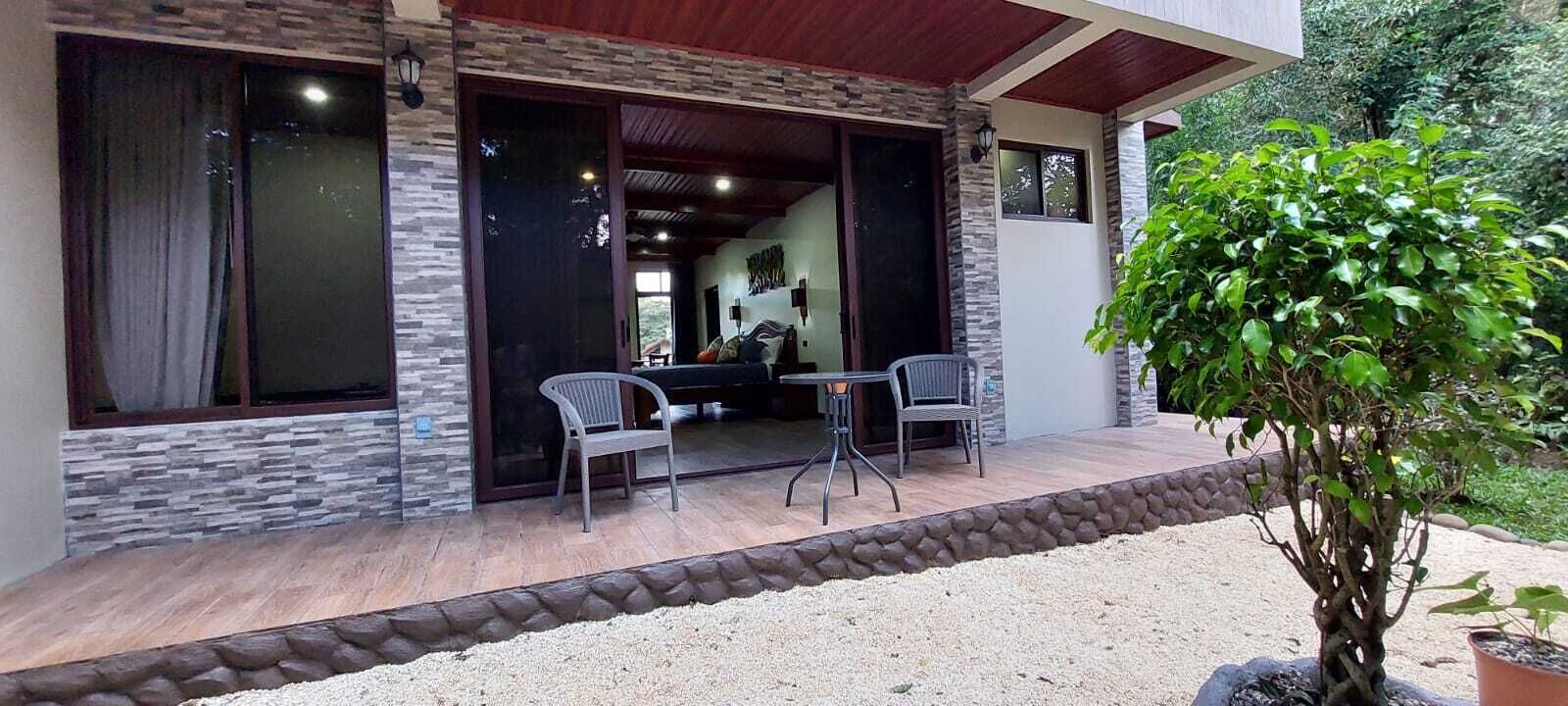 Un espacio de estar al aire libre cubierto con dos sillas, una mesa, un muro de piedra y una planta en maceta.