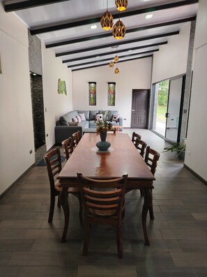 Un comedor amplio con una larga mesa de madera y sillas, un conjunto de sofás y lámparas colgantes.