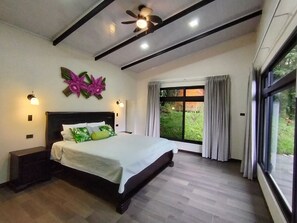 Un dormitorio con cama, ventilador de techo, luces fijadas a la pared y una ventana con cortinas.