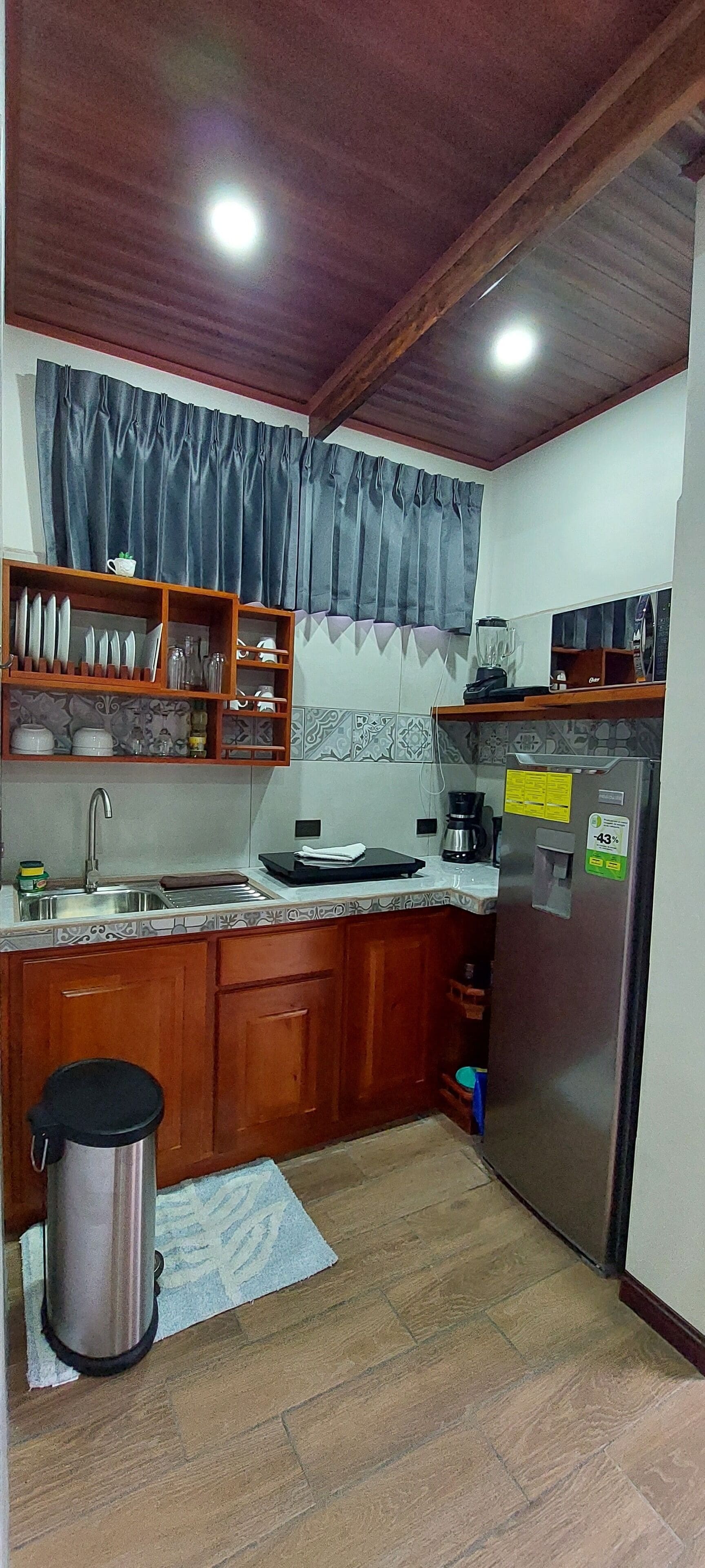 A compact kitchen with wooden cabinets, a stainless steel refrigerator, a sink, and a coffee maker.