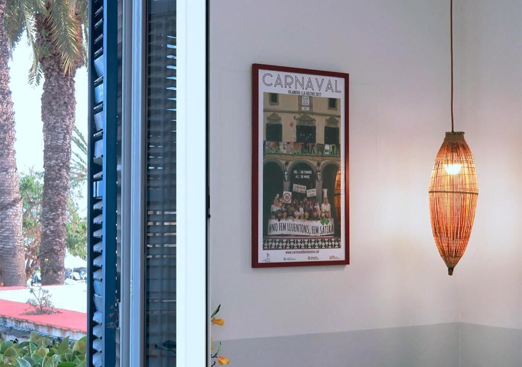 Een lijst met een affiche van een kermis, een hanglamp en een raam met jaloezieën.