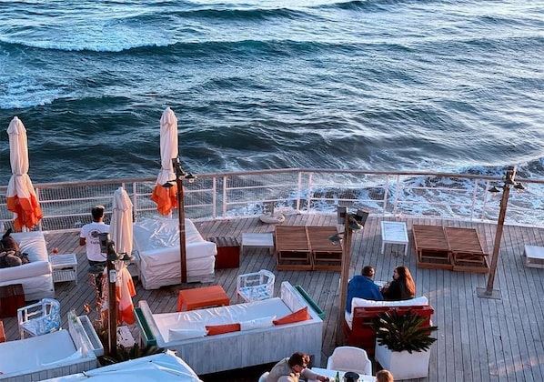 A deck with outdoor seating, umbrellas, and a view of the ocean.