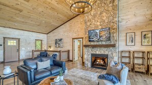 A spacious living room with a stone fireplace, wooden ceiling, and a large chandelier. - EPIC Pool * View * Outdoor Kitchen * Luxury (Mineral Bluff)