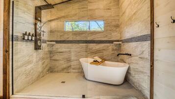 A modern bathroom with a freestanding bathtub, a shower area, and a window providing natural light.