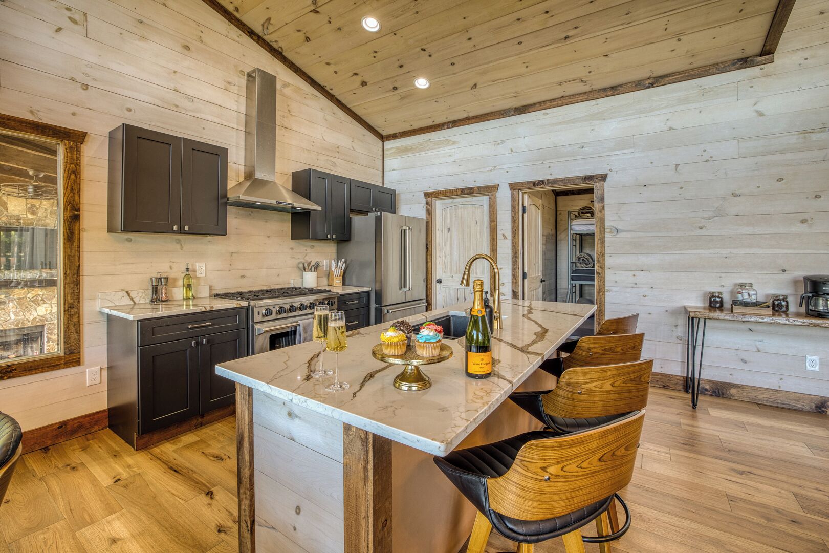 A kitchen with a central island, dark cabinets, a stainless steel range hood, and a wooden ceiling.