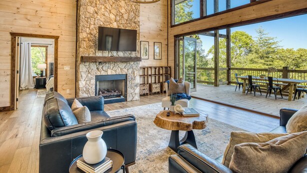 A spacious living room with a stone fireplace, leather sofas, and a large window overlooking a deck. - EPIC Pool * View * Outdoor Kitchen * Luxury (Mineral Bluff)