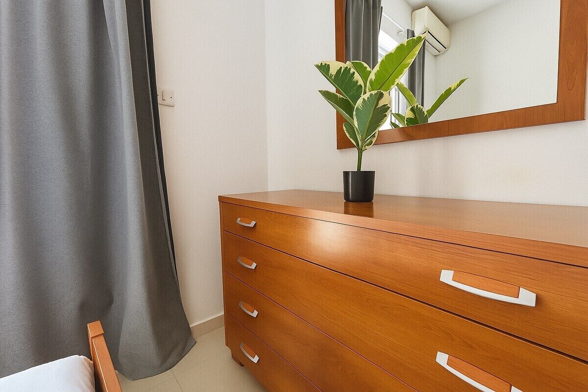 Une commode en bois avec quatre tiroirs, une plante en pot et un miroir.