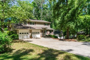 A two-story house with a garage, surrounded by lush greenery and trees.