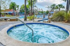 A hot tub area with a pool, surrounded by palm trees and umbrellas. - Cozy 4BR Resort Style Villa with Private Pool near Disney (Osceola County)