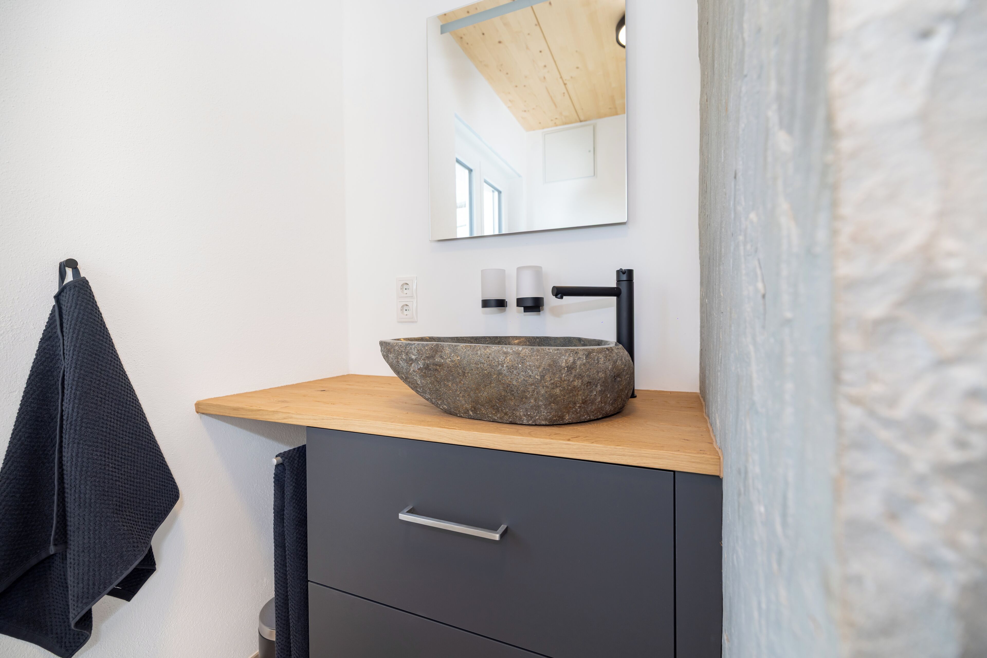 A modern bathroom with a stone sink, wooden countertop, and a mirror above it.