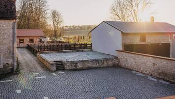 A courtyard with cobblestone flooring, a wooden fence, and a stone building with a red roof.