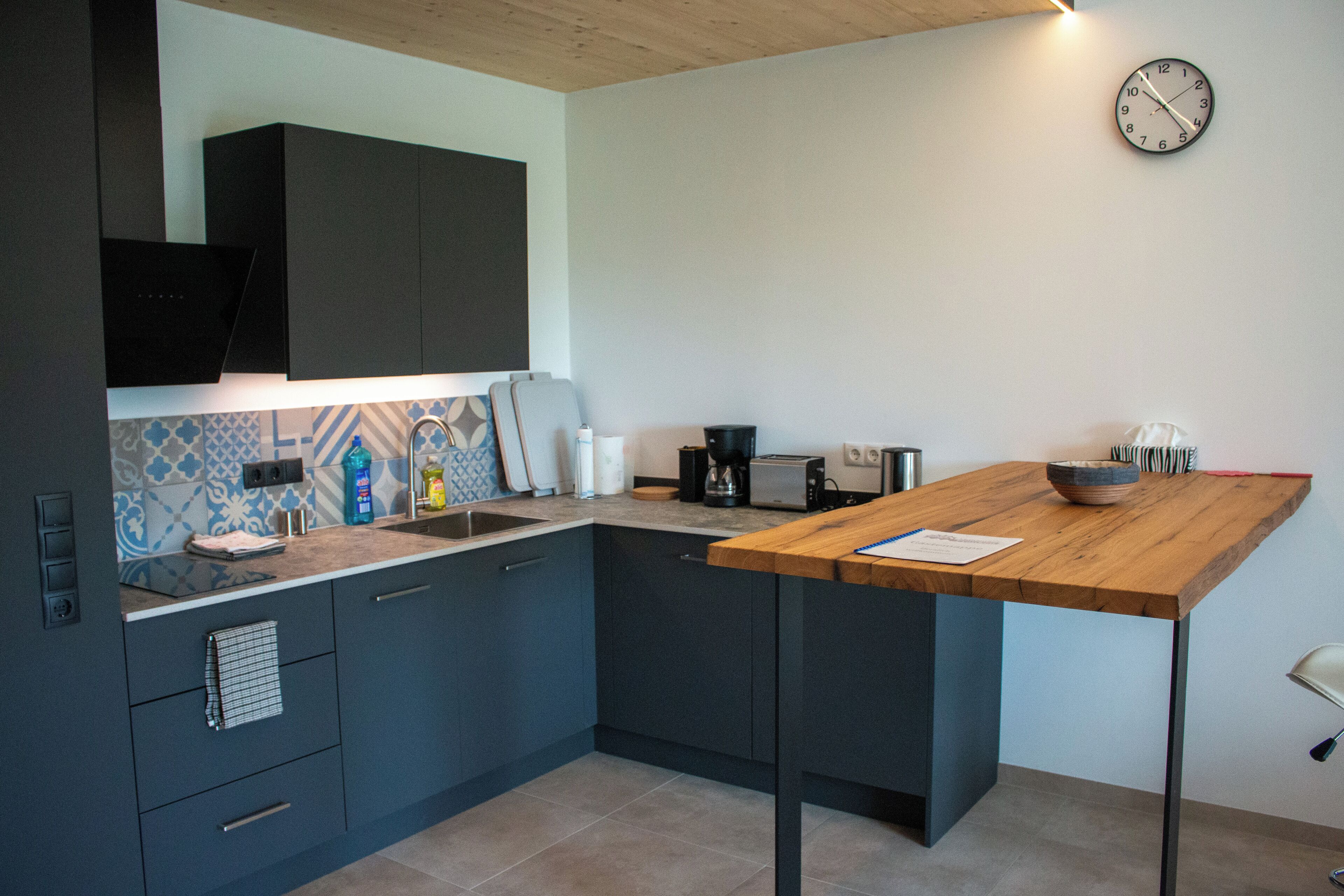 A modern kitchen with dark blue cabinets, a wooden countertop, and a built-in oven.