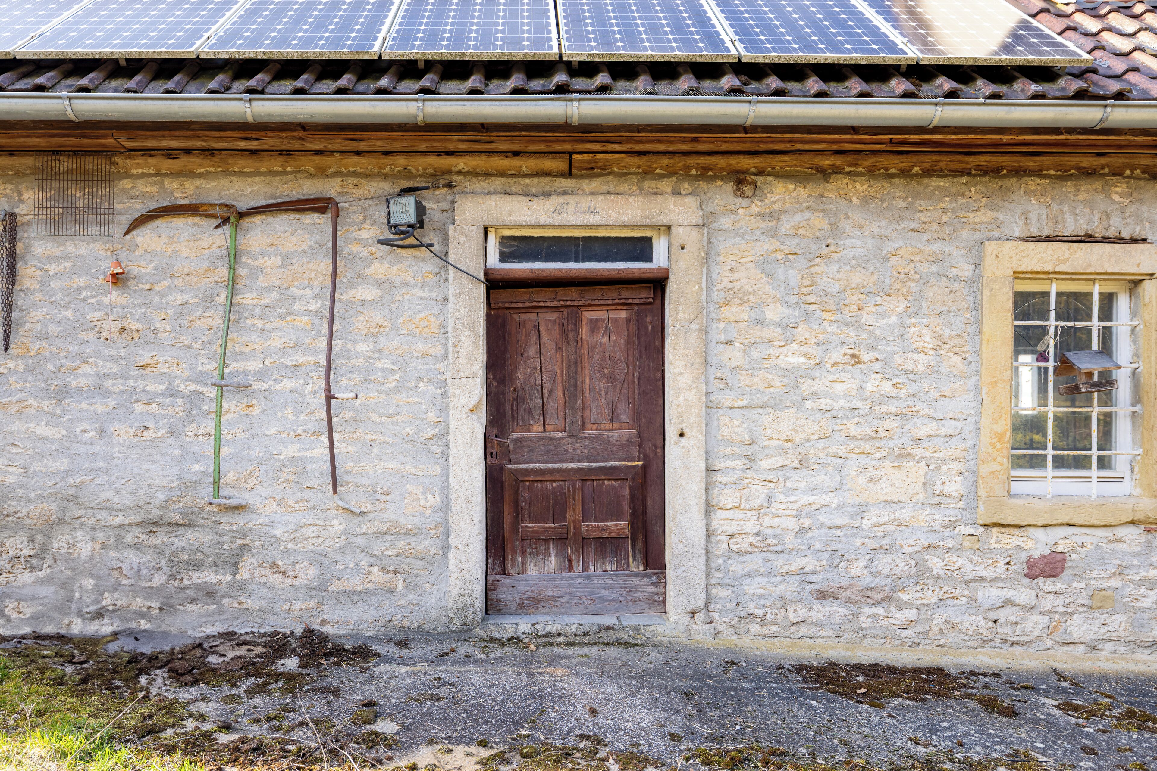 A rustic stone building with a wooden door, a small window, and a solar panel on the roof.