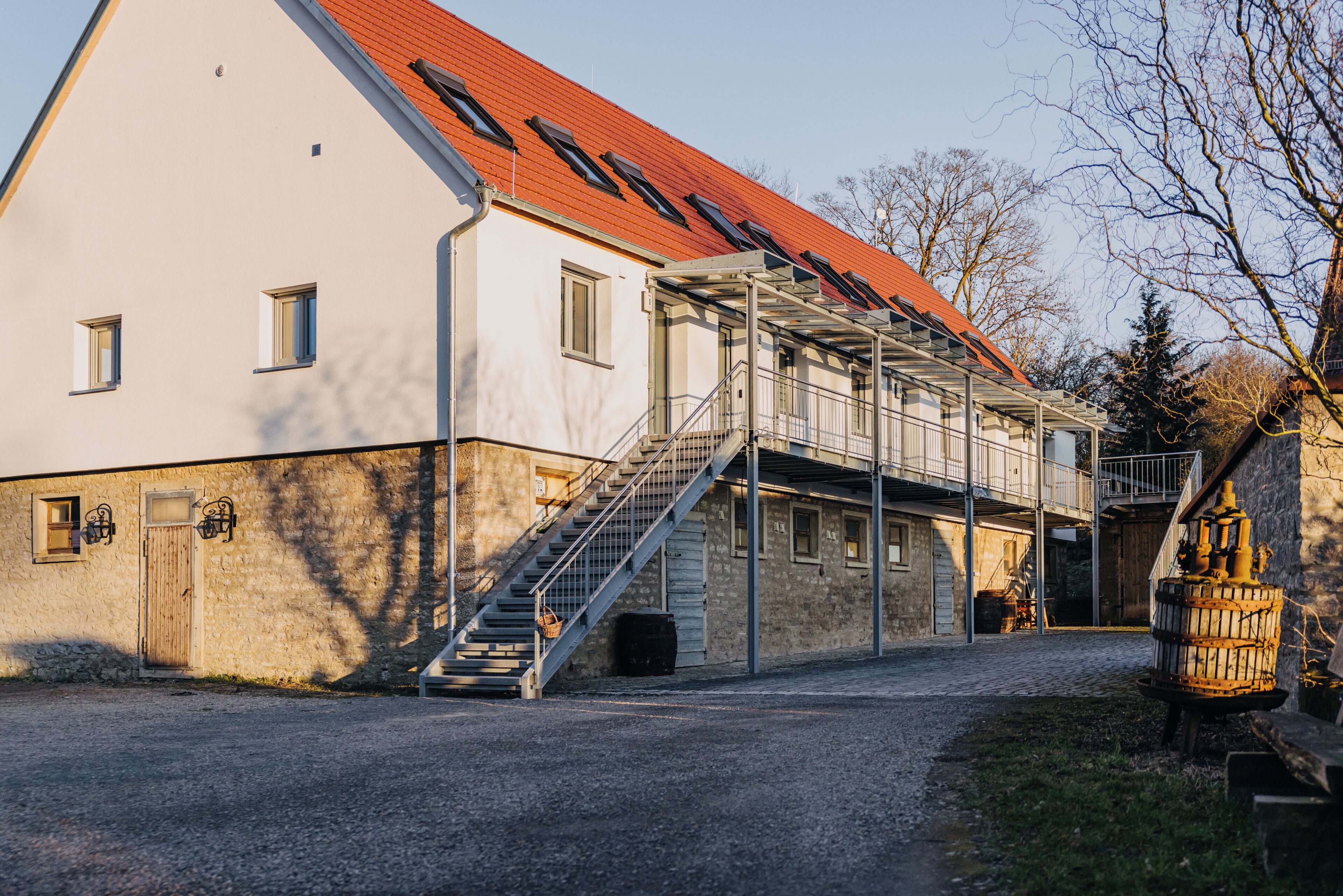 A building with a sloped roof, a staircase leading to a covered area, and a gravel driveway.