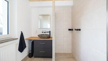 A modern bathroom with a stone sink, dark cabinetry, a wooden ceiling, and a large mirror.