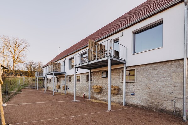 A building with multiple balconies, a stone facade, and a dirt ground area. - Mühlenhof Franken (Kirchheim)