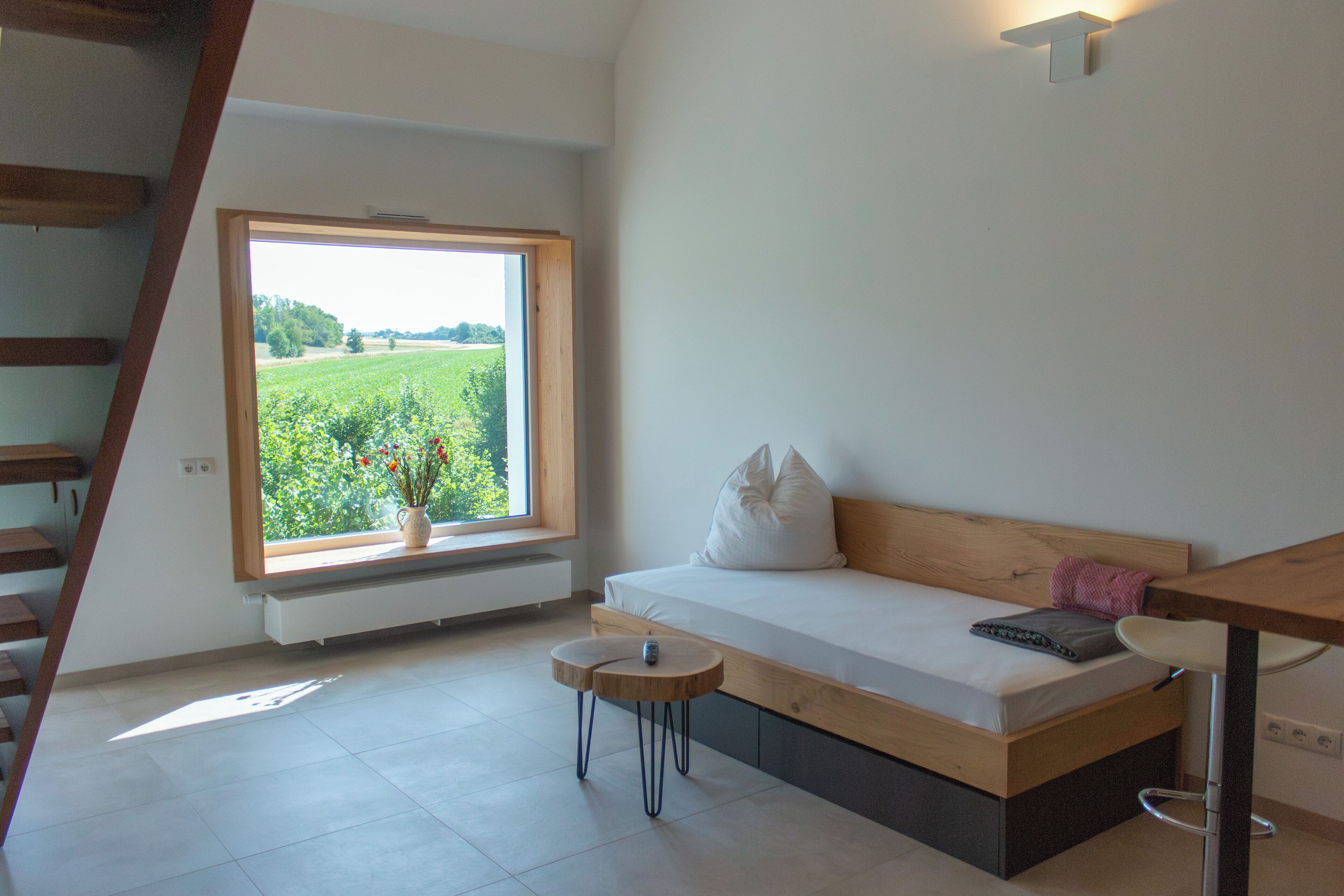 A modern bedroom with a wooden bed, a small round table, and a window with a view of a green field.