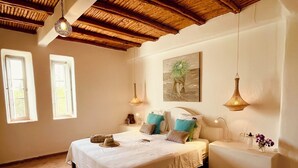 Une chambre à coucher comprenant un lit, des tables de chevet, un banc, un tableau et deux lampes suspendues.