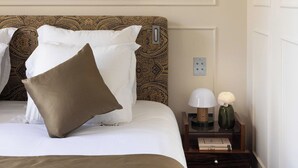 Un lit bien fait, avec une literie à motifs, une table de chevet avec une lampe et un vase, et un grand tableau abstrait accroché au mur.