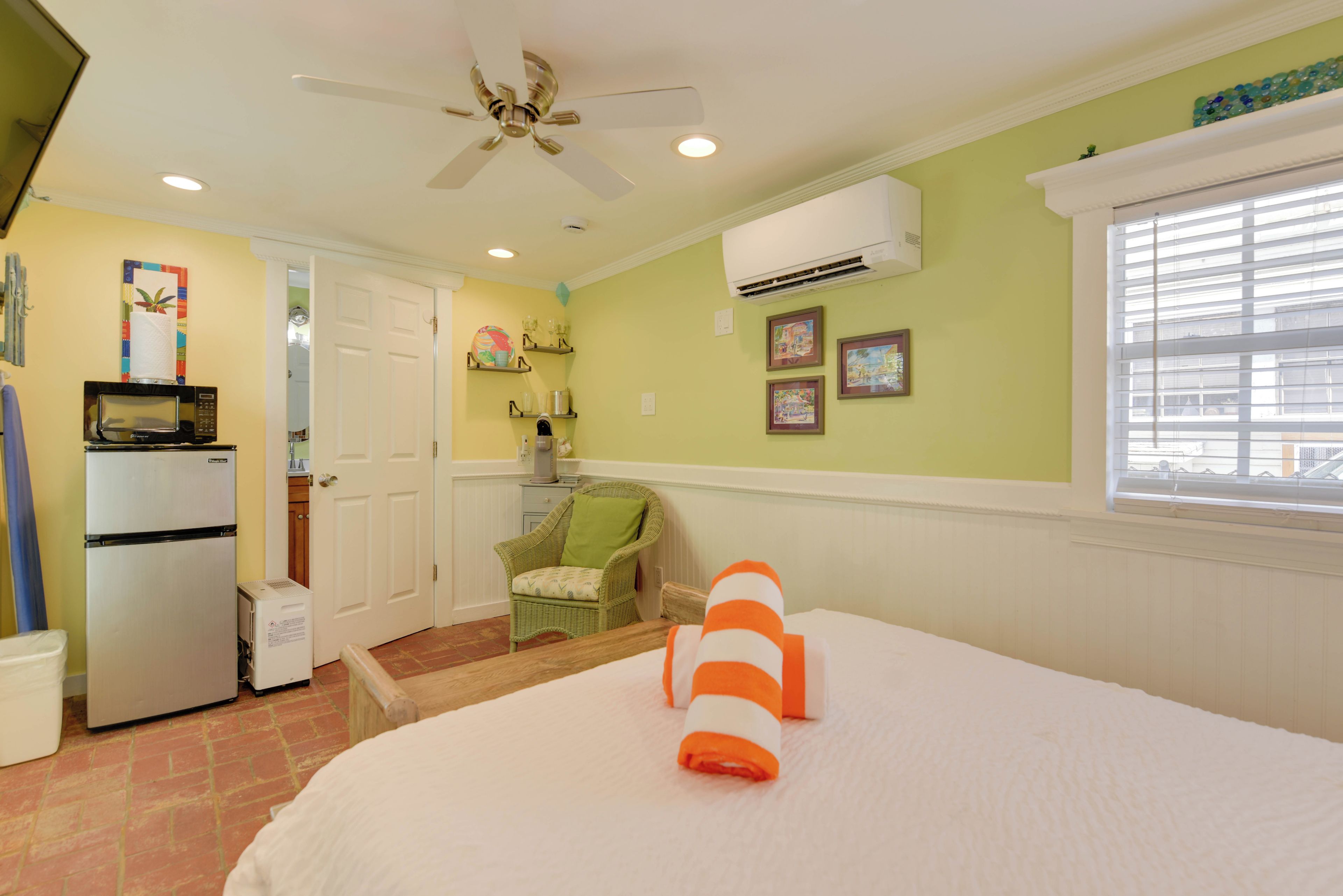 Une chambre d’hôtel équipée d’un lit, d’un ventilateur de plafond, d’un four à micro-ondes, d’un réfrigérateur, d’une chaise et d’une fenêtre avec des stores.