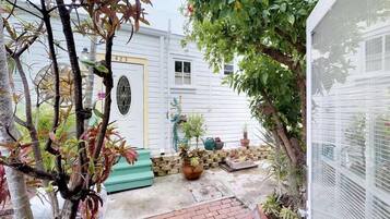 Un petit jardin clos, avec une maison blanche, une porte jaune et diverses plantes en pot.