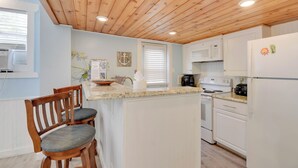 A kitchen with wooden ceiling, white cabinets, a microwave, stove, and two bar stools. - Welcome Matt's - Truman @ Duval | Perfect Hideaway! (Key West)